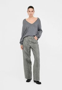 Gray v-neck sweater with long sleeves paired with wide-leg gray jeans featuring a subtle animal print pattern. Minimalist black shoes.