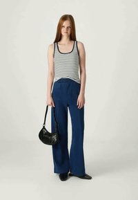 Débardeur rayé en blanc et marine, associé à un pantalon large bleu. Sac à épaule noir avec une forme courbée et une courte bandoulière. Chaussures noires.
