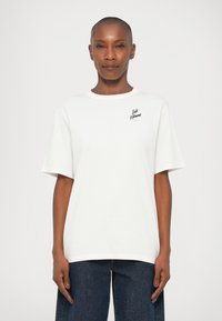 T-shirt bianco a maniche corte in cotone con scollatura a girocollo, caratterizzato da un piccolo logo nero stampato sul lato sinistro del petto. Vestibilità casual.