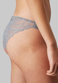 Culotte en dentelle de couleur bleu doux, avec un bord festonné et un motif floral complexe, en tissu transparent et finition lisse.