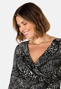 Abito a fantasia bianco e nero con scollatura a V profonda e tessuto drappeggiato. Presenta una superficie liscia e maniche lunghe. Accento con collana dorata.