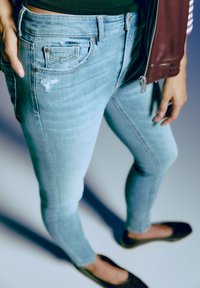 Svijetloplave traper skinny traperice s pohabanom detaljem na džepu. Glatka tekstura, uski kroj, srednji pojas, nosi se s crnim balerinkama.