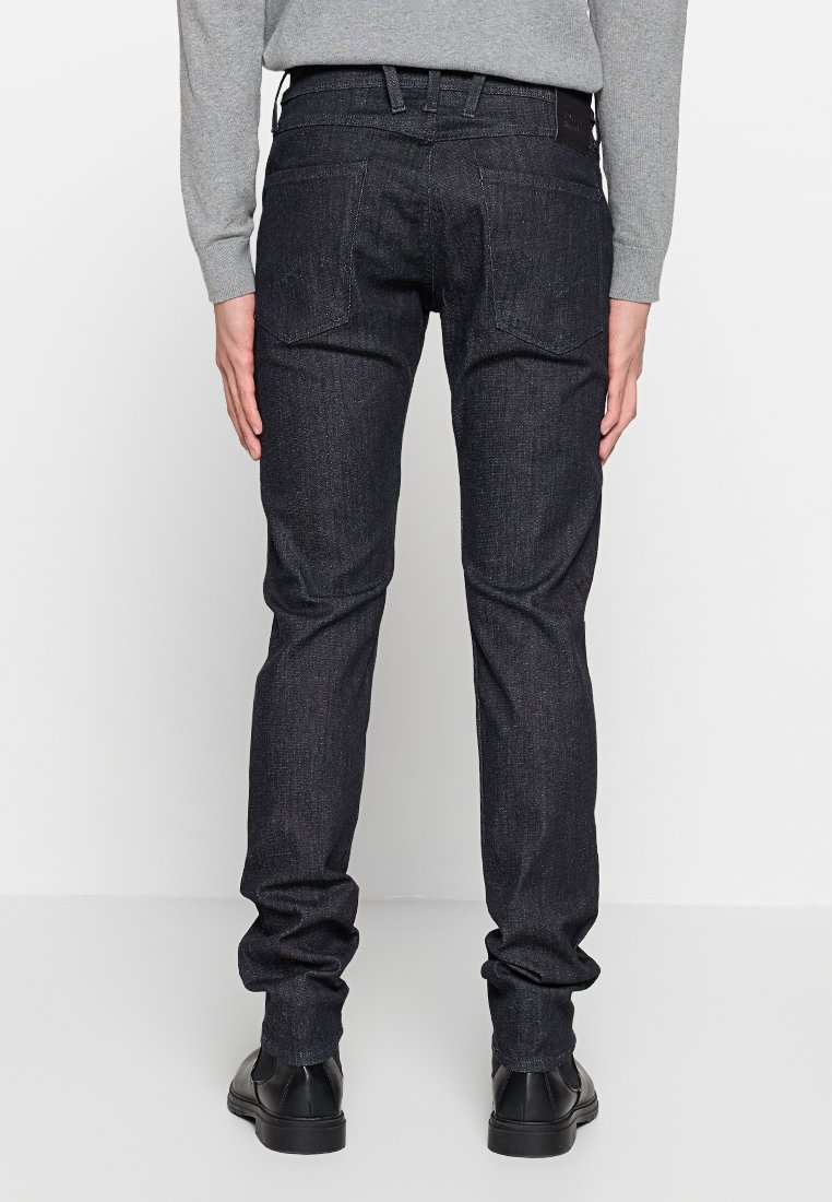 Herren-Jeans aus dunklem Denim mit geradem Schnitt, fünf Taschen und einem schwarzen Lederpatch am Bund. Der Stoff zeigt eine subtile Textur.