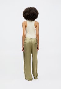 Haut sans manches beige avec texture côtelée ; pantalon large vert olive avec poches latérales et finition lisse. Vue de dos.