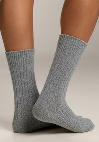 Calzini grigi a coste realizzati in materiale testurizzato, con altezza a metà polpaccio e design della punta senza cuciture, mostrati di lato.