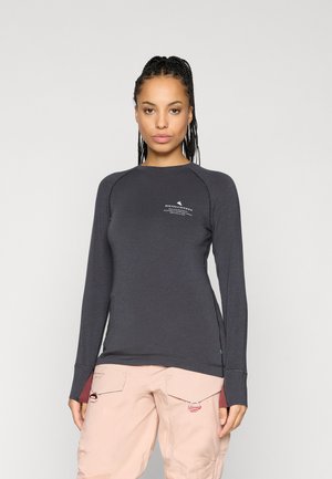 Chemise à manches longues, gris foncé, en tissu lisse, avec des manches raglan et un petit logo sur le haut à gauche. Coupe ajustée avec des fentes latérales.