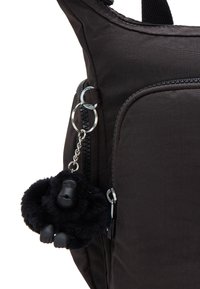 Black fabric bag featuring a sleek design and zippered compartments, adorned with a fuzzy black gorilla keychain for added detail.