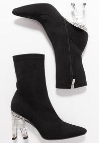 Bottines noires à talon transparent avec des orteils pointus, dotées de zips latéraux et d'un dessus en tissu lisse.