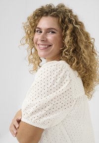 Hvid bluse med perforeret tekstur, puffærmer og sammensnørede manchetter. Let og luftig design med en afslappet silhuet.