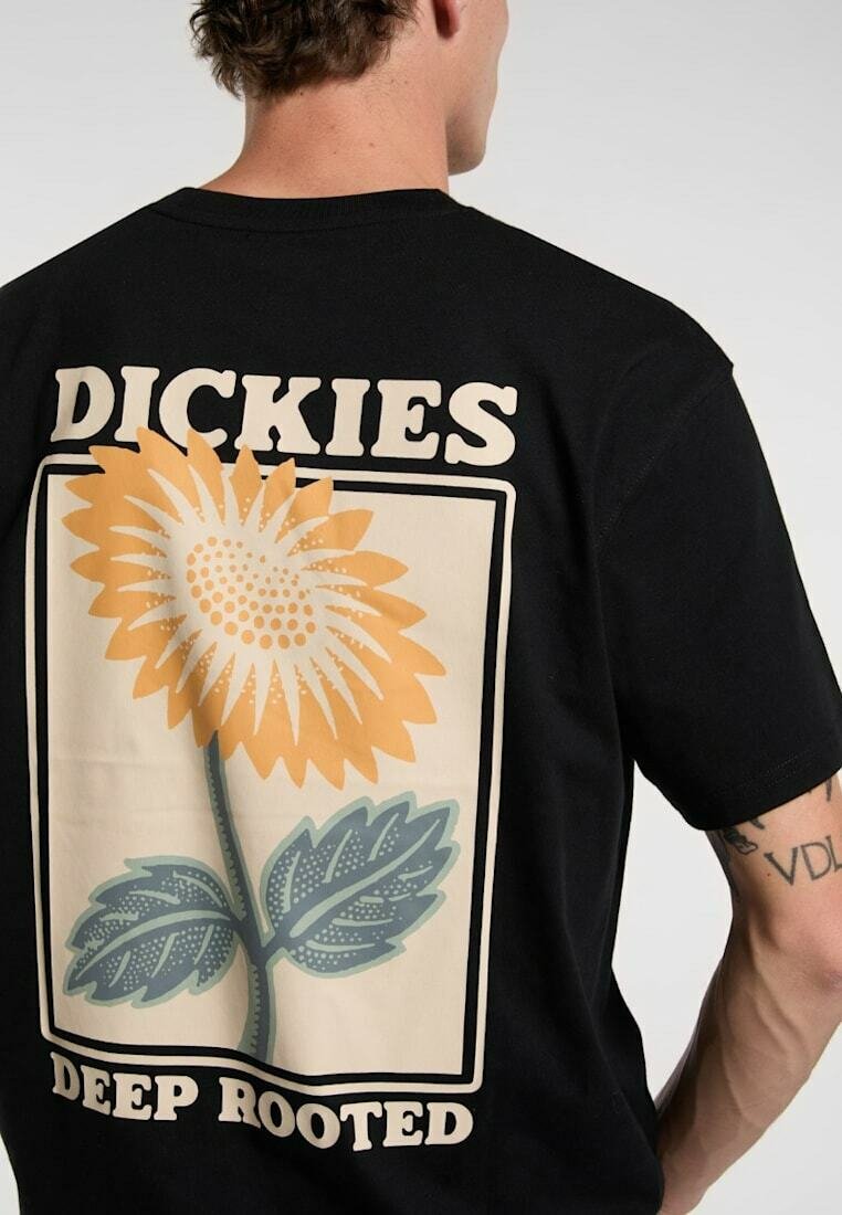 Person iført en sort t-shirt med en stor solsikke-grafik og teksten "DICKIES" over og "DEEP ROOTED" under blomsten på ryggen.