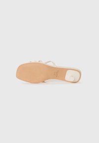 Beige høye hælsandaler med tynne remmer, en glatt lærøvre og en lys tan gummisåle med hvit detalj på hælen.