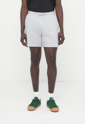 Γκρι βαμβακερά σορτς με ελαστική μέση και κορδόνι. Συνδυάζονται με πράσινα αθλητικά παπούτσια και λευκές κάλτσες. Απλός, καθημερινός σχεδιασμός.
