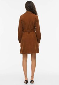 Robe en velours côtelé marron avec manches longues, col chemise et taille ceinturée. Elle présente une jupe évasée et un tissu texturé.