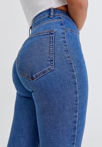 Jean en denim bleu taille haute avec une coupe ajustée, poches arrière et un léger délavage sur le tissu pour une variation de texture.