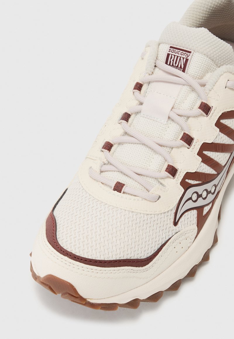 Sneaker bianco in mesh con dettagli marroni, tessuto testurizzato, collo imbottito e rifiniture riflettenti. Suola in gomma con tacchetti per la trazione.