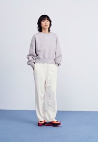 Grå sweatshirt med vit Nike-logga, krämfärgade byxor och svarta/rosa chunky sneakers. Slät tyg med avslappnad passform och elastisk midja.