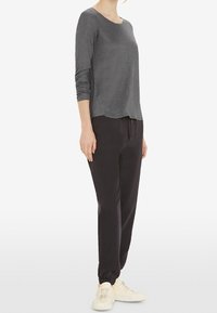 Graues Langarmshirt mit rundem Halsausschnitt, kombiniert mit schwarzen Jogginghosen mit elastischen Bündchen und weißen Sneakers.