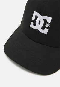 Zwarte honkbalpet met een gebogen rand, voorzien van een wit geborduurd DC-logo en sterontwerp. De stof lijkt glad met een gestructureerde vorm.