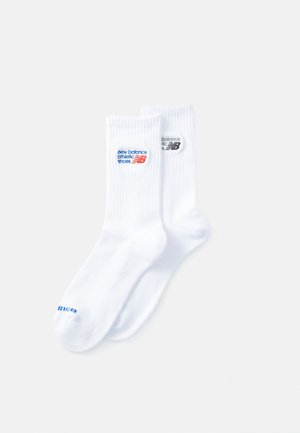 Chaussettes côtelées blanches avec des logos "New Balance Athletic Shoes" en bleu et noir. Le tissu est doux et flexible avec un design de longueur mi-mollet.