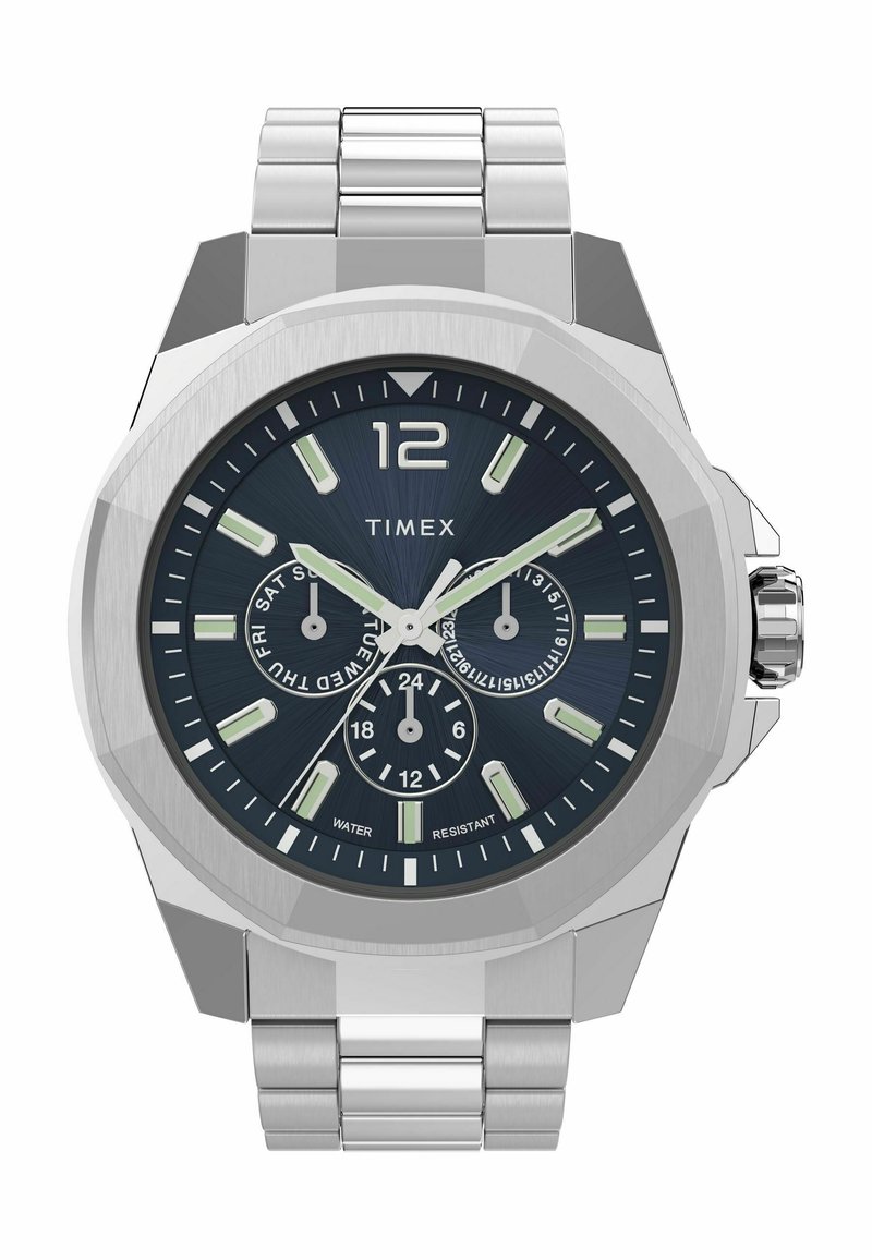 Montre en métal argenté avec un cadran bleu foncé, des index horaires proéminents, trois sous-cadrans et une lunette texturée. Équipée d'un bracelet en acier inoxydable.