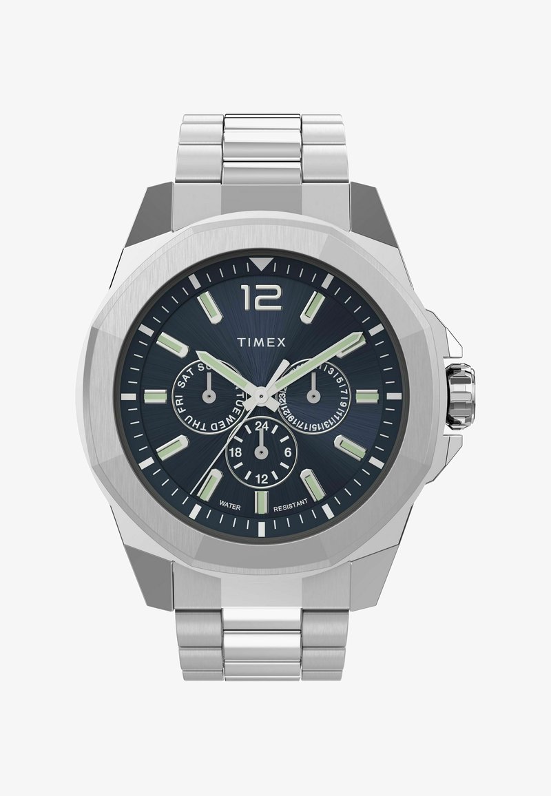 Montre en métal argenté avec un cadran bleu foncé, des index horaires proéminents, trois sous-cadrans et une lunette texturée. Équipée d'un bracelet en acier inoxydable.