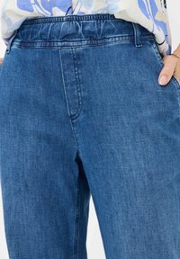 Blue denim pants featuring an elastic waistband, side pockets, and a relaxed fit. The fabric has a smooth texture and subtle fading.