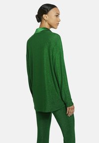 Grünes glitzerndes Loungewear-Set mit einem locker sitzenden Langarmhemd mit Satin-Kragen und passenden engen Hosen.