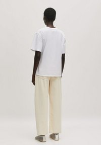 Witte katoenen t-shirt met korte mouwen, gecombineerd met ruime crèmekleurige broek. Schoenen hebben een zwart-wit geweven patroon.