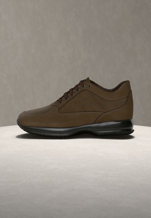 Hnedá kožená teniska s hladkou textúrou, zaoblenou špičkou a čiernou gumovou podrážkou. Má šnurovací predok a jemné švy.