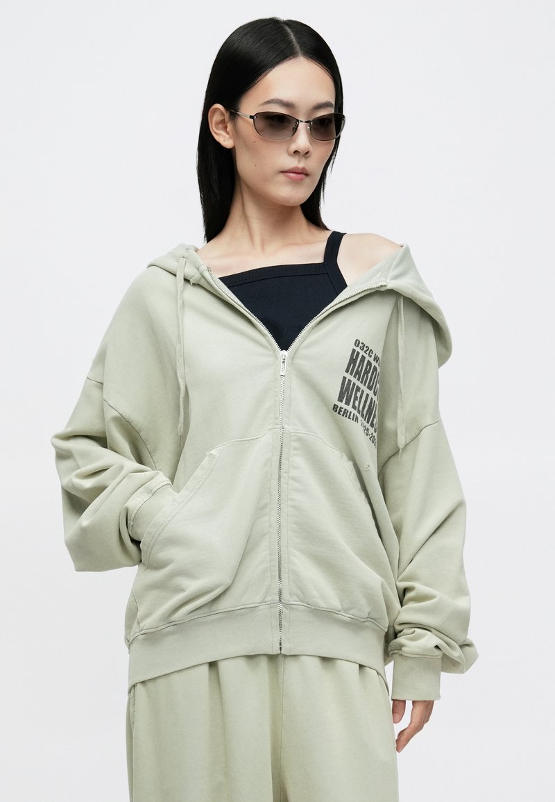 Lichtgroene zip-up hoodie met een losse fit, voorzien van een grafische print op de borst, grote zakken en een capuchon. Textuurstof met een casual ontwerp.