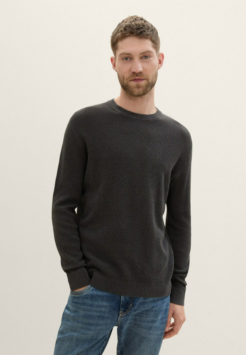 Suéter de punto gris oscuro con cuello redondo y mangas largas, combinado con jeans azules. Textura suave y diseño ajustado.