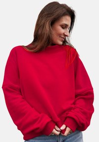 Czerwona, oversize'owa bluza z ribbowanym dekoltem i ściągaczami, wykonana z miękkiego materiału. Posiada opuszczone ramiona dla swobodnego kroju.