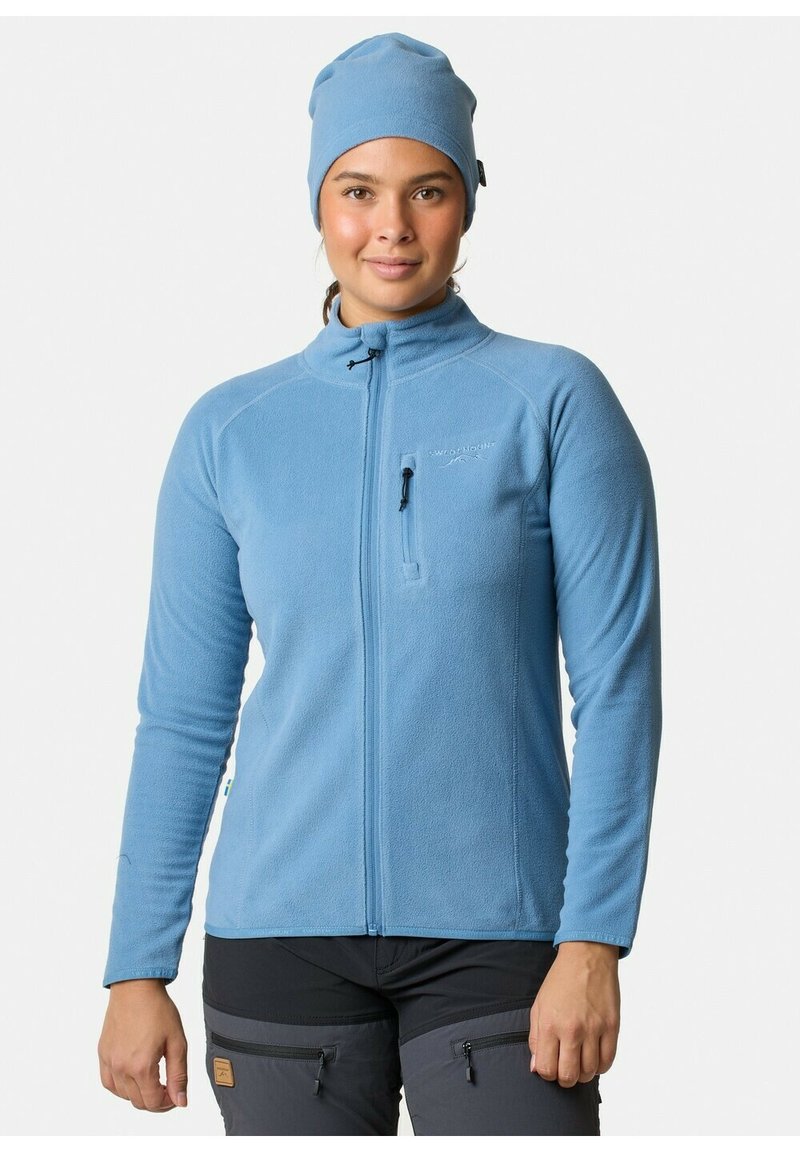 Giacca in felpa blu chiaro con colletto alto, zip completa e taschino sul petto. Indossata con un berretto coordinato, presenta maniche lunghe e un design aderente.