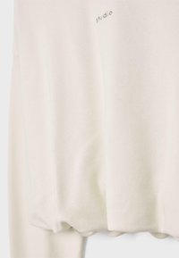 Sweat-shirt écru avec petit texte "studio" imprimé près du haut de la poitrine, avec un ourlet détendu légèrement froncé.