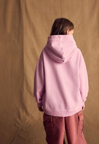 Felpa oversize rosa con cappuccio regolabile, polsini e orlo a coste, abbinata a pantaloni cargo marrone chiaro dalla vestibilità ampia.