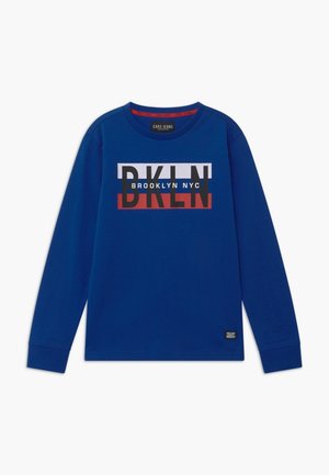 Blå langærmet skjorte med rund hals, med "BKLYN" i store bogstaver og "BROOKLYN NYC" tekst over brystet.