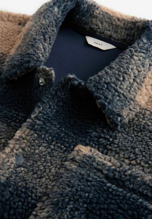Fleece jacket featuring a gradient of navy and beige colors, with a textured surface and snap button closure at the collar.