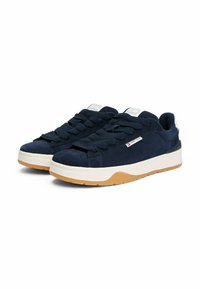 Sneakers in suede blu navy con lacci spessi blu navy, imbottitura bianca sul tallone e suola in gomma testurizzata per una migliore presa. Presentano un'etichetta con logo bianco.