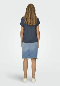 T-shirt bleu foncé à manches courtes associé à une jupe en denim bleu clair avec un ourlet effiloché. Des baskets blanches complètent la tenue.