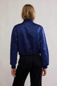 Námořnicky modrá bomber bunda z atlasu s texturovaným povrchem, žebrovanými manžetami a límcem. Zkrácená délka s raglánovými rukávy a elastickým pasem.