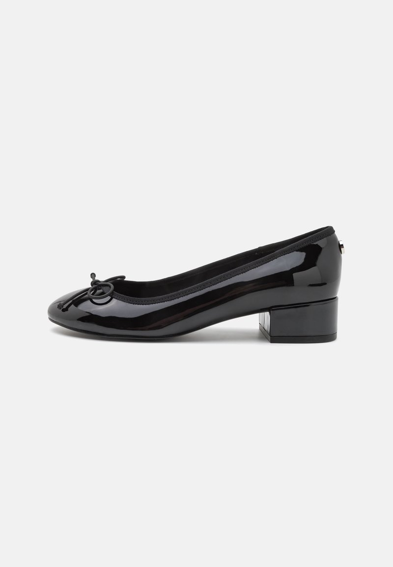 Ballerine à talon bas en cuir verni noir avec bout arrondi et petit nœud décoratif sur le dessus, vue de côté sur fond blanc.