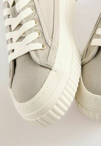 Sneakers in tela grigia chiara con accenti crema, dotati di lacci piatti e una suola in gomma testurizzata con un motivo a righe.
