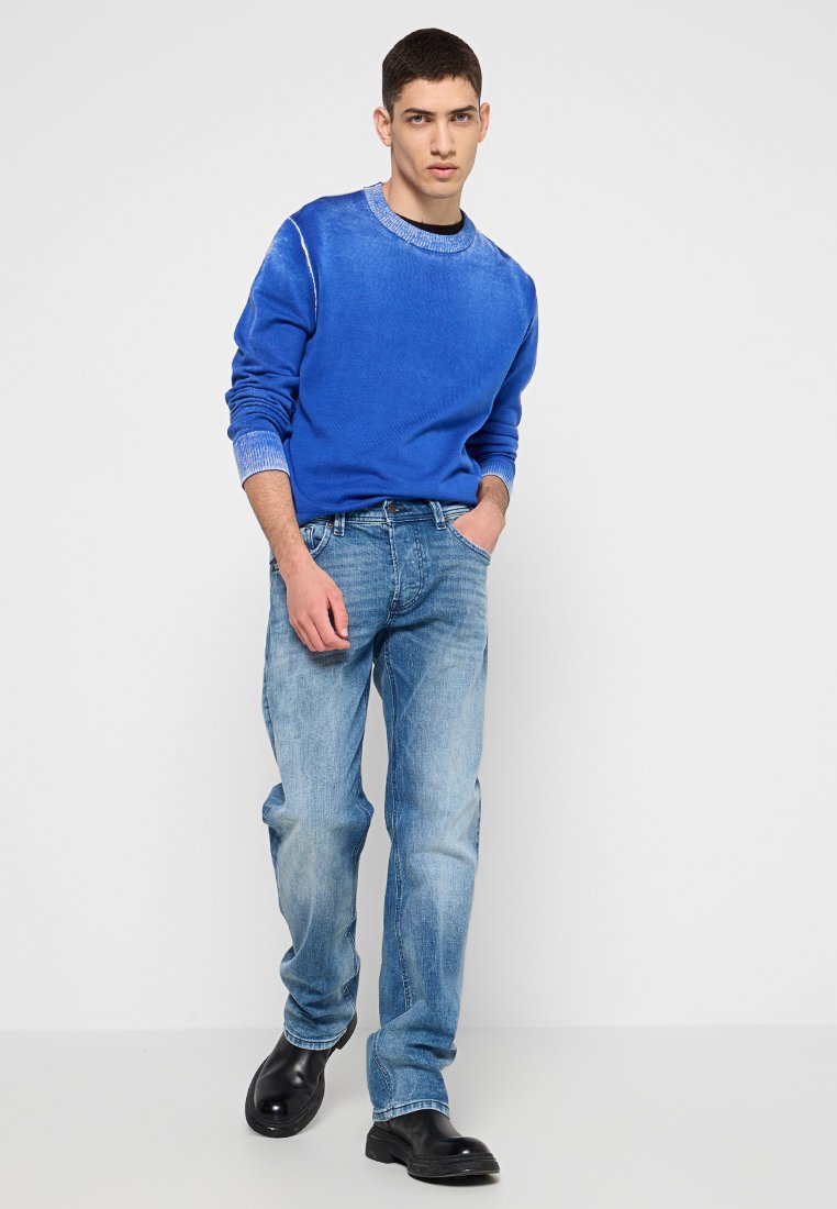 Maglione blu a maglia con scollatura rotonda e polsini lavorati, abbinato a jeans in denim azzurro chiaro. Calzature nere completano l'outfit.
