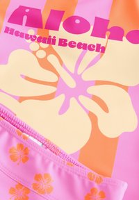 Színes fürdőruha, rózsaszín és narancssárga virágmintával, boldog rózsaszín „Aloha Hawaii Beach” felirattal, őszibarack háttérrel.