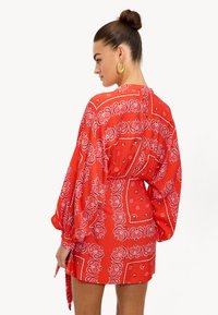 Vestido corto rojo con estampado de paisley, que cuenta con mangas largas y un detalle de cintura atada. Fabricado con una tela ligera y con un acabado texturizado.