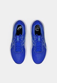 Siniset urheilukengät, joissa on tekstiilinäköinen päällinen, valkoinen pohja, pyöreä kärki ja nauhaketju. Sisältää hienovaraisia vihreitä yksityiskohtia ja logon kielekkeellä.