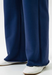 Marineblauwe, wijd gesneden broek met een gestructureerde afwerking en een contrasterende geweven zoom, gecombineerd met witte schoenen met platte zolen.