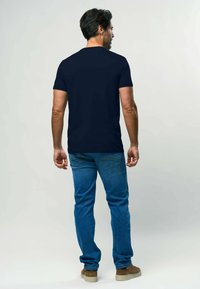 Tumši zila īsām piedurknēm T-krekls no kokvilnas, apvienots ar gaiši ziliem džinsiem un brūnām zamšādām kurpēm. Vienkāršs dizains, bez redzamām logo.