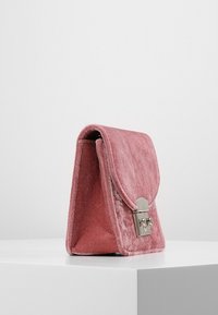 Borsa in velluto rosa con pattina e hardware argentato. La borsa presenta una forma strutturata e una consistenza morbida, poggiando su una superficie bianca.
