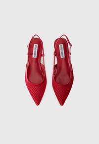 Escarpins slingback rouges avec un bout pointu et un design en maille texturée et ouverte. Bride ajustable avec boucle, doublure intérieure lisse et semelle plate.
